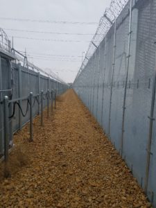 In between two long stretches of high security fencing, one stretch being almost twice as tall as the other